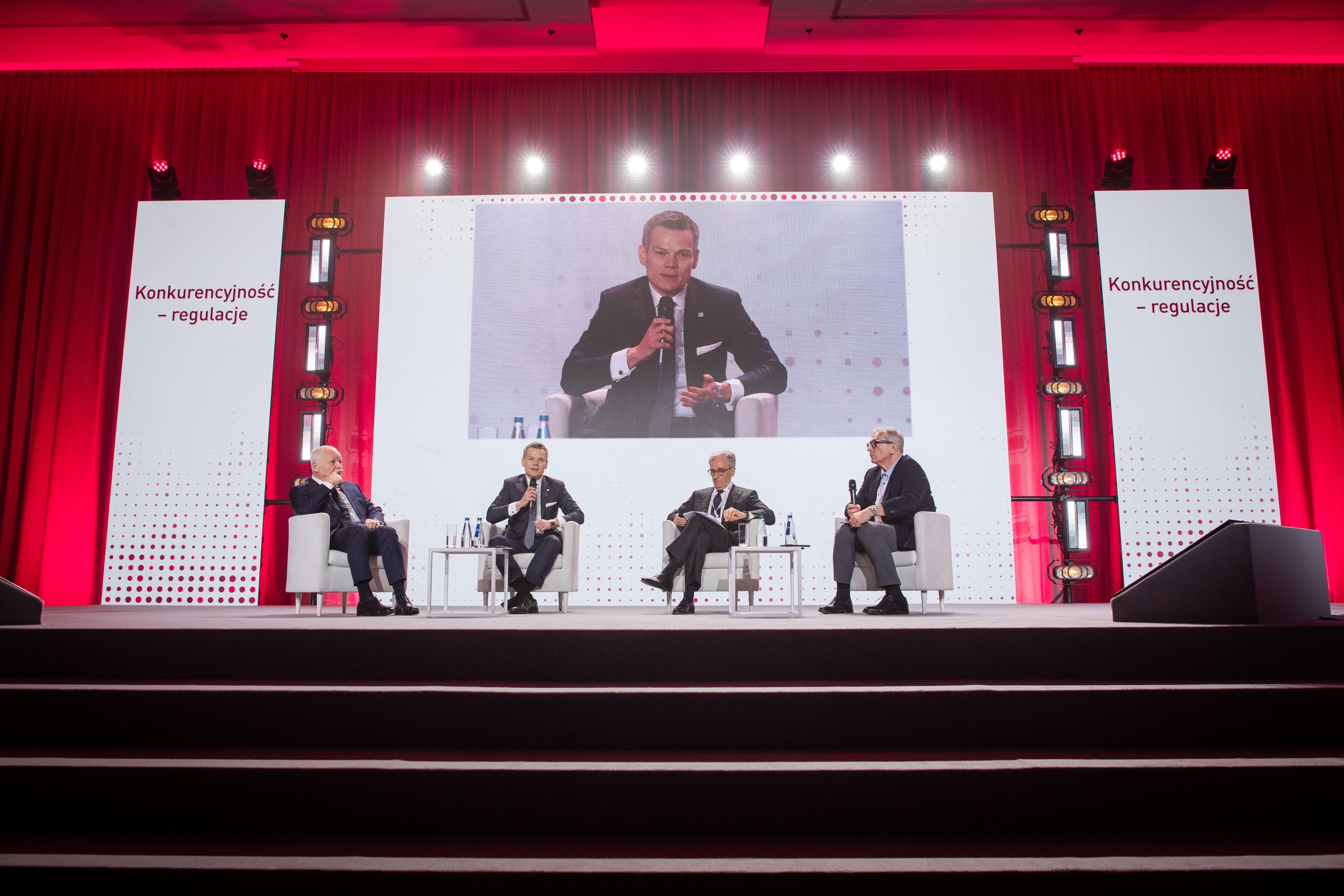 debate participants on stage and photo of Jacek Jastrzębski on screen